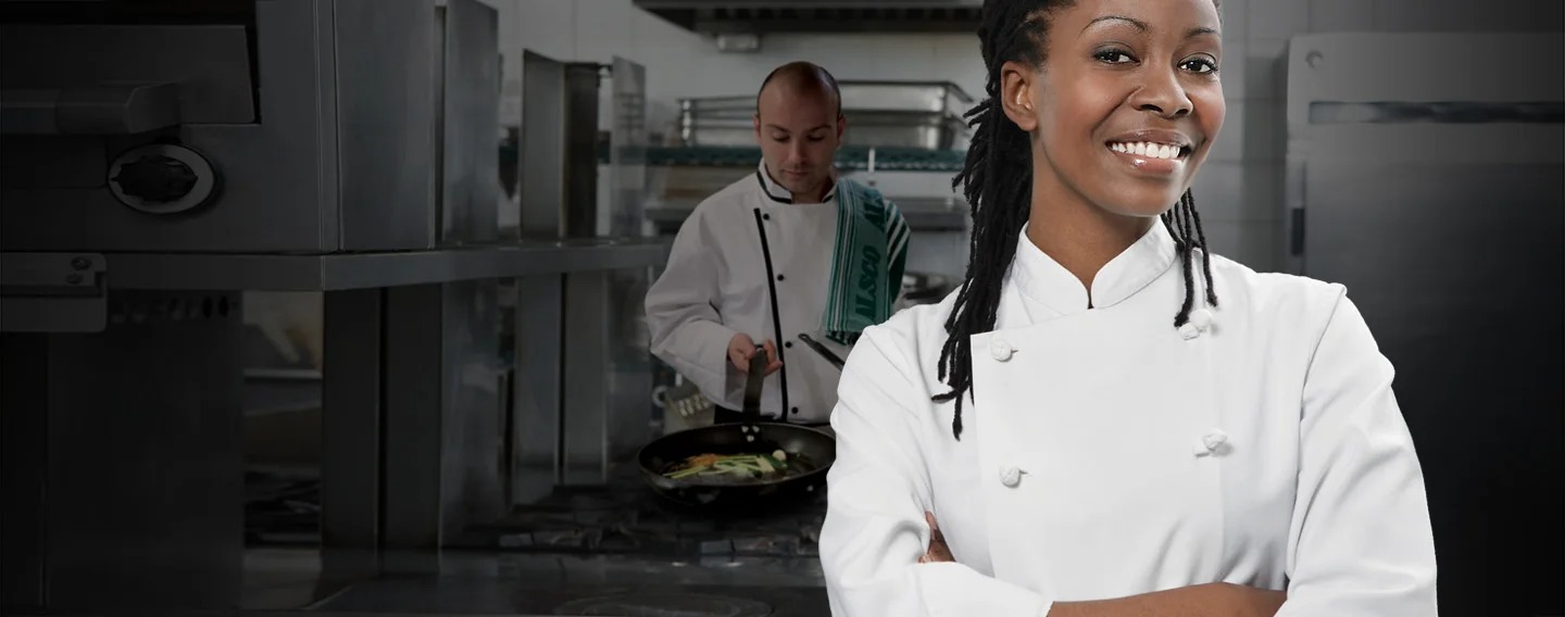 Un chef souriant devant un autre chef travaillant avec une casserole